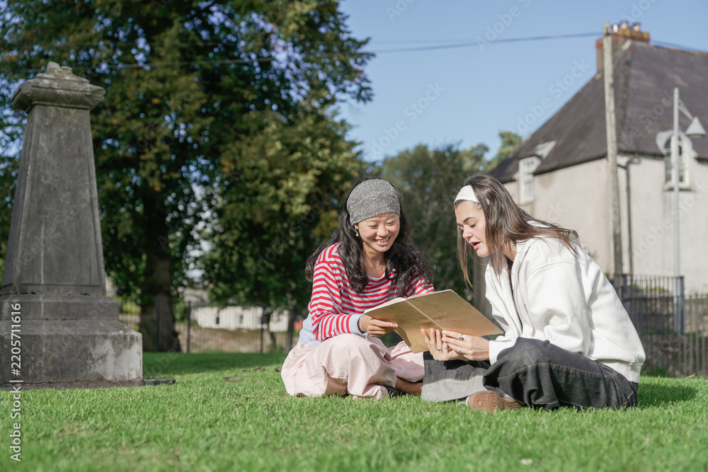 Obraz premium Young women studying book together in a cemetery