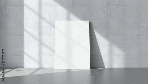 Blank white poster frame leaning against a grey concrete wall with natural sunlight shadows from a window
