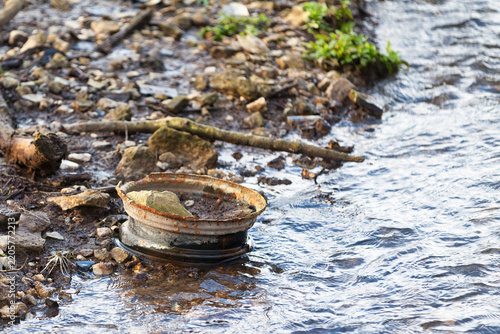 Rusted car rim abandoned on a riverbank
