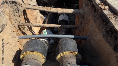 New pre-insulated district heating pipes in an open street trench, camera tilts up to a fenced urban roadworks site on a sunny day
