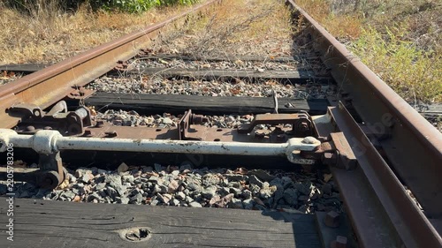 Low angle view moving over a rusty railroad switch to a long perspective of an overgrown, disused track under a blue summer sky