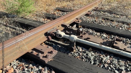 Rusty railroad switch on wooden sleepers and gravel, camera moves along the overgrown track to an old manual switch lever in sunlight