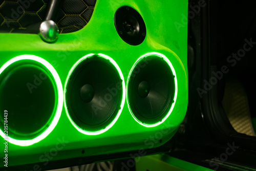 Neon green speaker panel with three illuminated circular drivers and textured black trim in a dramatic automotive audio installation close up