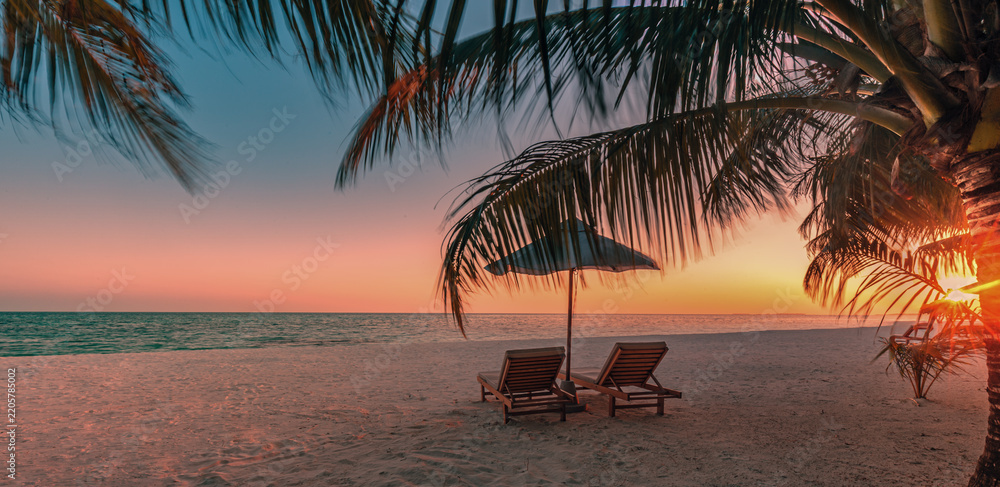 Obraz premium Romantic sunset tropical beach palm trees sunbeds umbrella glowing golden sky calm sea sandy shore paradise. Perfect summer vacation travel scene. Luxury honeymoon couples relax love coastal getaway