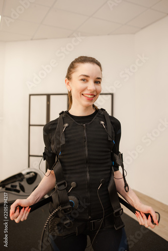 Foto Smiling woman in EMS suit ready for electrical muscle stimulation training indoo