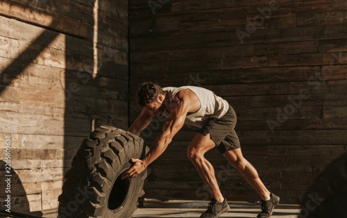 Strong Man Engaging in Functional Fitness Workout with Tire in Rustic Gym Setting