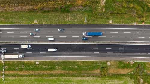 Aerial View of Highway Traffic: An aerial perspective captures the flow of vehicles on a multi-lane highway, with trucks and cars navigating the road amidst green rural landscapes.
