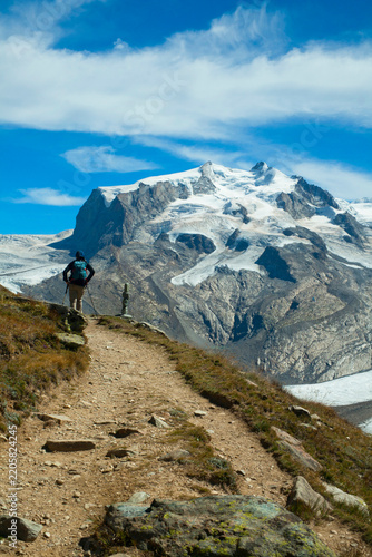 Hiker on Alpine Trail Overlooking Majestic Glacier and Snow-Capped Mountains