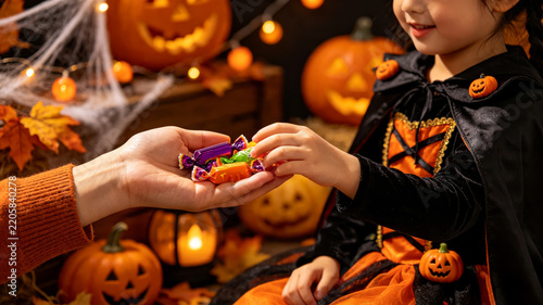 Cute Asian Girl in Halloween Costume Taking Colorful Candies from Adult Hand During Trick or Treat