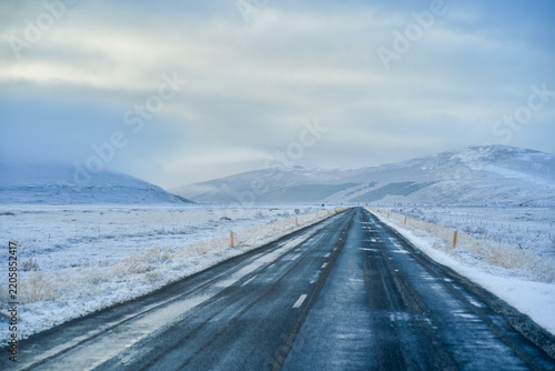 Scenic icy winter road driving in extreme conditions on the Iceland Ring Road. Snow-covered highway with mountain landscape and overcast sky.
