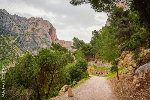 Gravel path leading past a stone aqueduct toward rocky peaks at Caminito del Rey