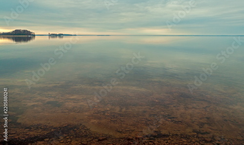 Eenokki, Finland - 20.04.2019: Calm lake with clear shallow water revealing a pebbly bottom under a soft overcast sky with distant islands