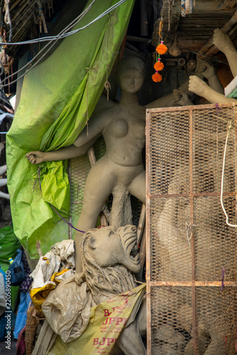 An unfinished clay idol of Goddess Durga inside a traditional workshop at Kumartuli, Kolkata, viewed through a heavy transparent plastic sheet hanging across the workshop front to shield the artwork 