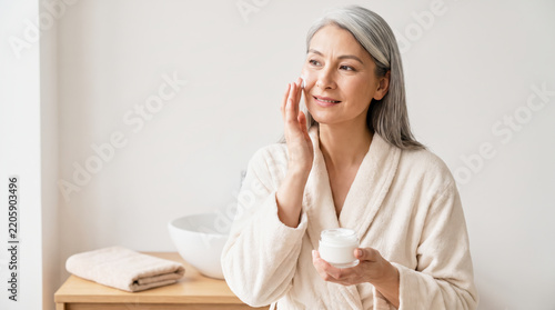 Mature Woman Applying Face Cream in Minimal Wellness Interior