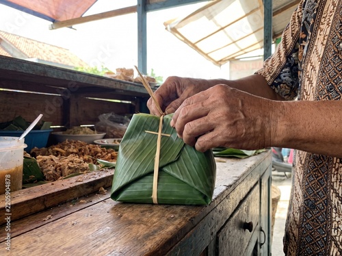 Hand of a man showing already wrapped food with banana leave 