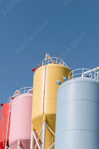 Pastel-colored industrial storage silos photographed from a low angle against a clear blue sky