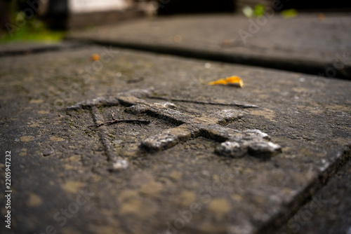 Carved stone cross relief on weathered ancient gravestone slab in old cemetery, representing christian funeral memorial, faith, and religious history.