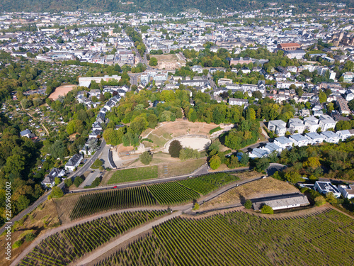 Aerial view of the historic Roman amphitheater in Trier, surrounded by lush vineyards, urban rooftops, and the scenic Moselle river valley in Trier, Rhineland-Palatinate, Germany.