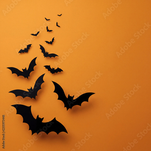 Black paper cutout bats flying upward across bright orange background creating festive halloween mood with shadows casting