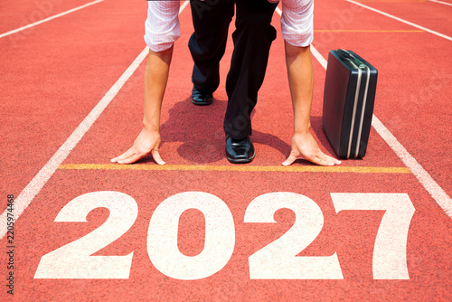 Business Man preparing to run on athletics track engraved with the year 2027