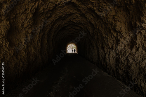 Two hikers silhouetted at the end of a rock tunnel on the Caminito del Rey trail
