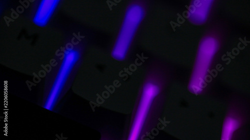 Close up of glowing RGB keyboard keys in blue and purple light, blurred gaming technology background