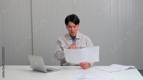 ノートパソコンと図面で作業を進める作業服の男性