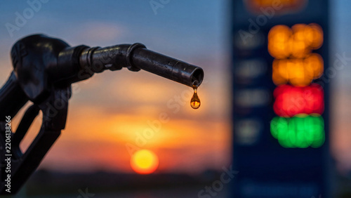 Fuel pump nozzle dripping oil drop at sunset, gas station price display background, energy crisis and petroleum industry photo