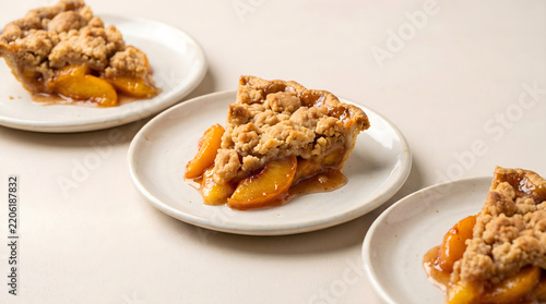 Three slices of homemade peach cobbler pie with a golden crumbly streusel topping served on individual white plates