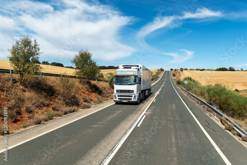Refrigerated truck driving on a rural road through farmland