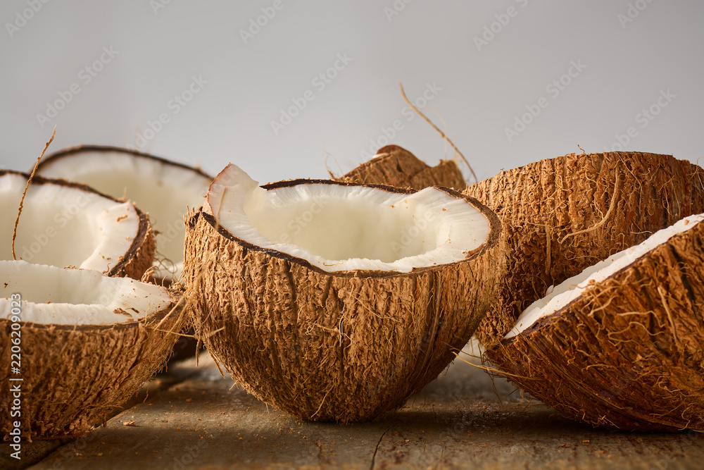 Obraz premium broken coconut halves on rustic wooden table, brown hairy shell and white fresh meat tropical fruit in close-up side view with copy space, healthy vegan food ingredient