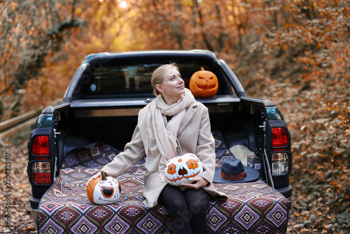 Autumn road trip with a woman, colorful Halloween pumpkins and a pickup truck, combining outdoor leisure and festive creativity.
