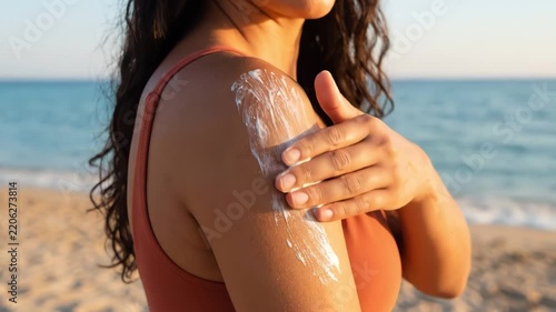 Woman applying sunscreen lotion on her shoulder on sandy beach at sunset