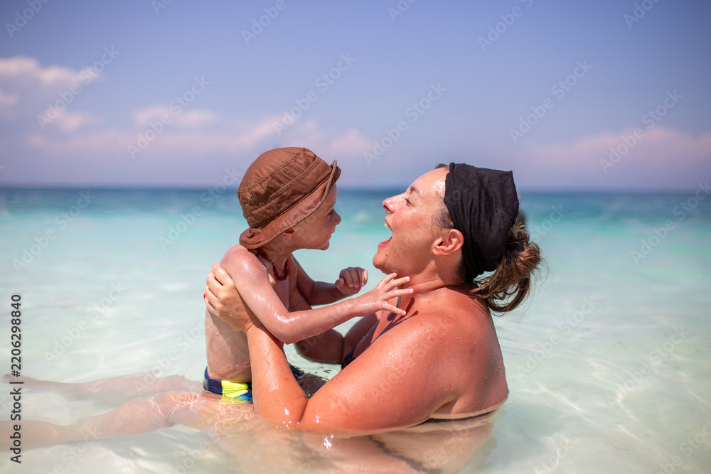 Fototapeta premium Mother and young son playing together in shallow sea during summer vacation