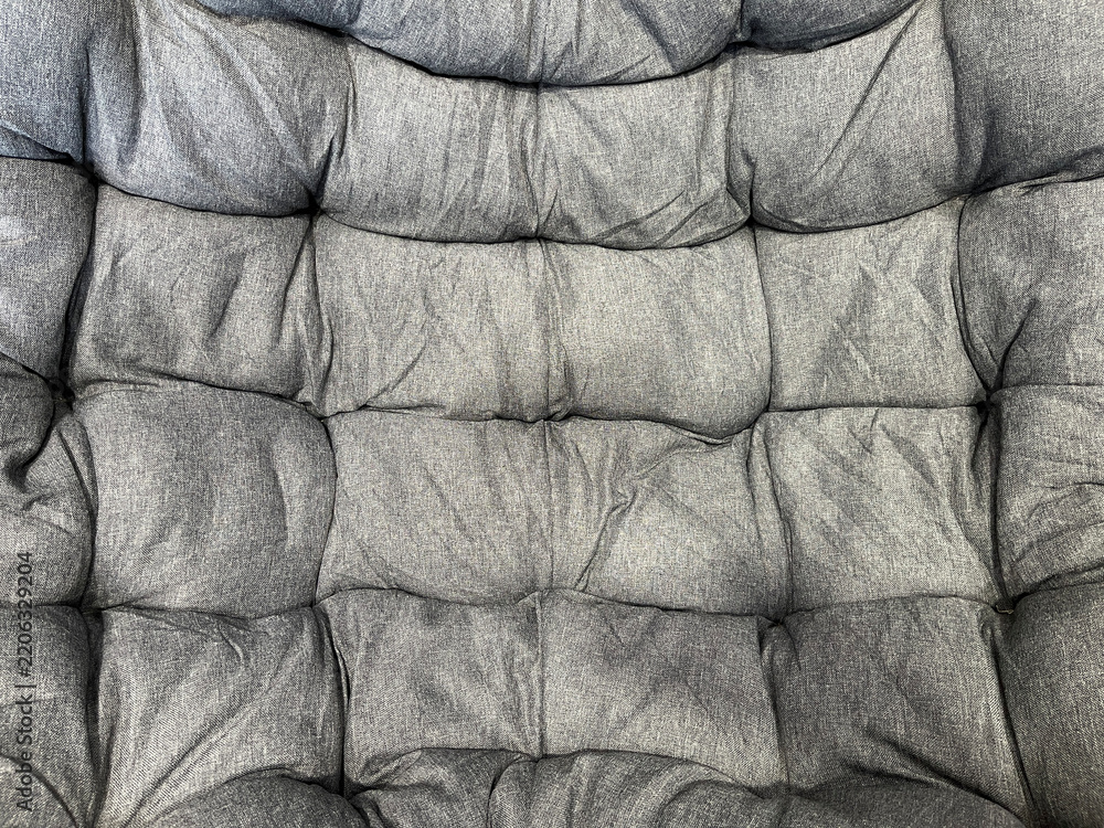 Fototapeta premium Close-up of a gray tufted fabric cushion with soft folds, stitched sections, and textured upholstery, creating a cozy abstract background pattern.