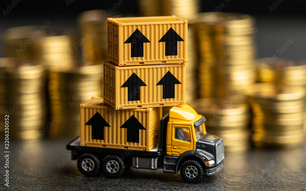 Obraz premium Yellow cargo containers with black up arrows stacked on miniature semi truck. Gold coin stacks form background. Concept of import tariff increase, rising trade costs, growing logistics expenses