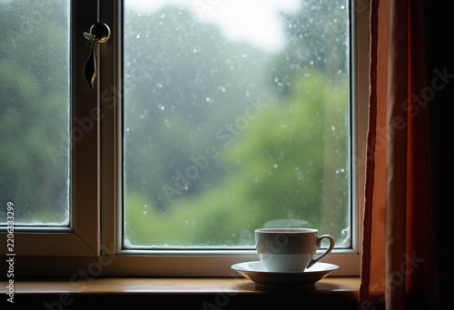 Window with rain outside, cup of tea on windowsill, cozy mood