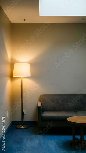 Quiet circulation space featuring a warm indirect floor lamp illuminating a plain textured wall, with its physical process or state transition clearly visible for relaxation, hospitality