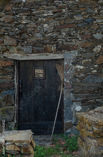 Ancient black door with a small window and a handmade wooden broom, halloween