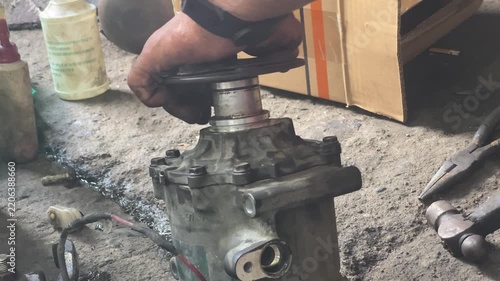 technician is assembling pieces of a broken car air conditioning compressor on the pavement.
