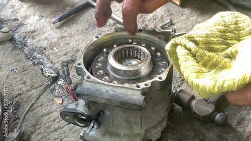 technician is assembling pieces of a broken car air conditioning compressor on the pavement.