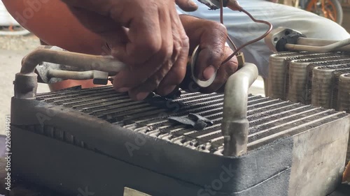 technician is assembling pieces of a broken car air conditioning evaporator on the pavement.