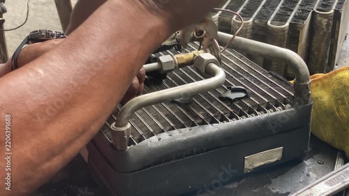 technician is assembling pieces of a broken car air conditioning evaporator on the pavement.