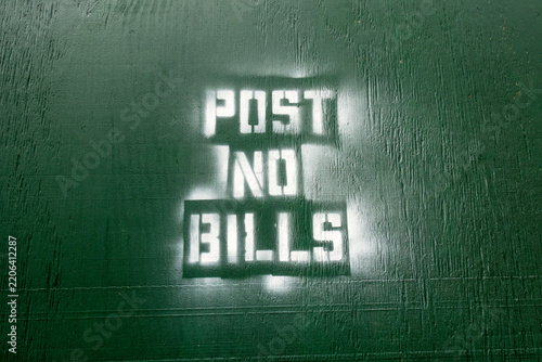 “Post No Bills” spray painted in white against a dark green wood background
