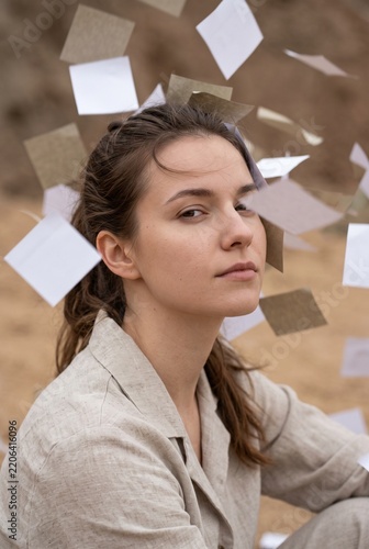 Thoughtful young woman surrounded by floating blank paper notes in a conceptual outdoor portrait depicting ideas and thoughts