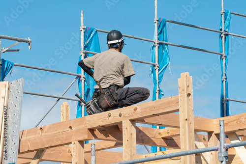 新築木造住宅の上棟。梁の上で建方作業をする大工職人の後ろ姿