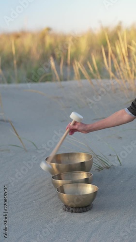 Hand playing singing bowls on sandy dunes at sunset