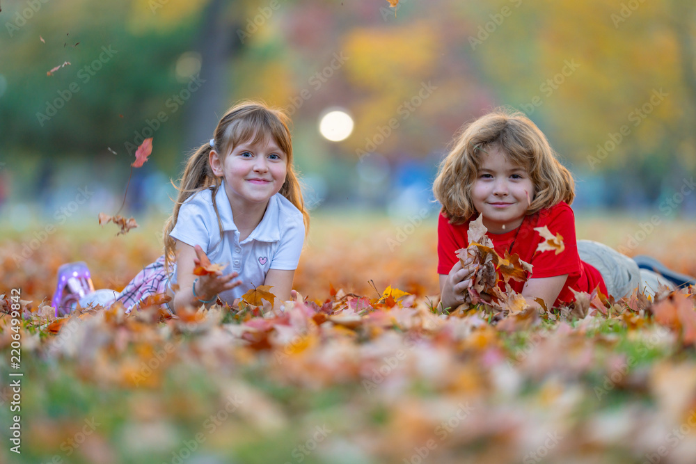 Fototapeta premium Autumn leaves near happy kids. Children smile on fallen foliage. Leaves fly during tossing. Play brings carefree fun. Laughing girl looks at boy. Friendship scene in park.