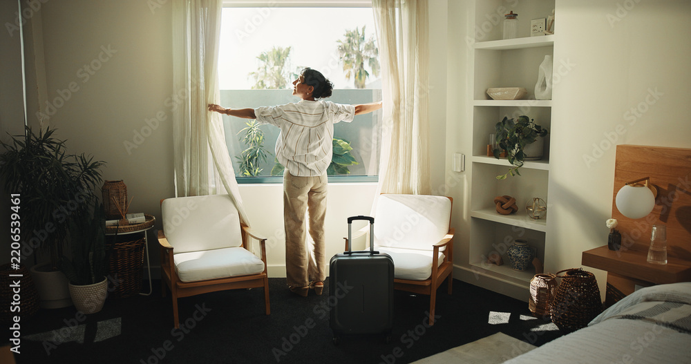 Fototapeta premium Window, curtain and happy woman with suitcase in hotel for holiday getaway, travel or vacation. Back, mature person and relax with sunshine for weekend or morning stay in luxury bedroom or resort