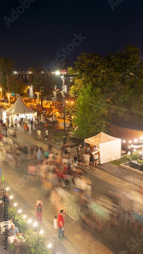 Budapest promenade night market timelapse with festive illuminated tents, riverside street scene, and blurred crowds moving along Danube